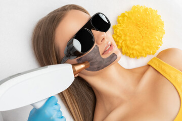Cosmetologist doing carbon peeling procedure to beautiful girl in a spa salon. Hardware cosmetology...