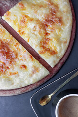 close-up cut piece of georgian khachapuri on a wooden kitchen board on a dark table. National traditional Georgian cuisine. a cup of black coffee is on the table. view from above.