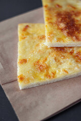 Two pieces of khachapuri on paper bags lie on a black table. Georgian traditional national cuisine.