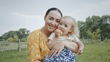 Portrait of a happy mother with her daughter in her arms in a summer park against the background of green trees and blue sky. The concept of happy motherhood and female maternal beauty.