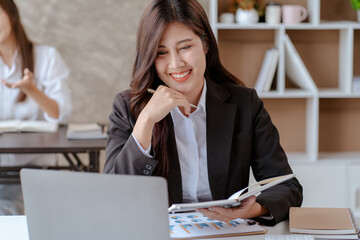 Happy young Asian businesswoman sitting on her workplace in the office. Young woman working at laptop computer in the office