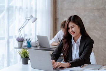 Happy young Asian businesswoman sitting on her workplace in the office. Young woman working at laptop computer in the office