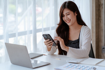 Happy young Asian businesswoman sitting on her workplace in the office. Young woman working at laptop computer in the office