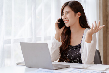 Happy young Asian businesswoman sitting on her workplace in the office. Young woman working at laptop computer in the office