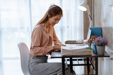 Happy young Asian businesswoman sitting on her workplace in the office. Young woman working at laptop computer in the office