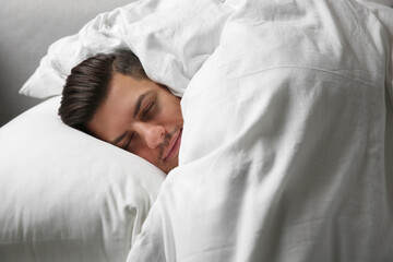 Handsome man sleeping under soft blanket in bed at home