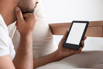 Man using e-book reader on sofa indoors, closeup