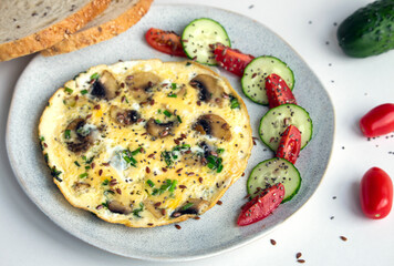Lunchtime omelette with mushrooms, green onion and dill with sliced tomatoes, cucumber and bread aside seasoned with chia and flax seeds