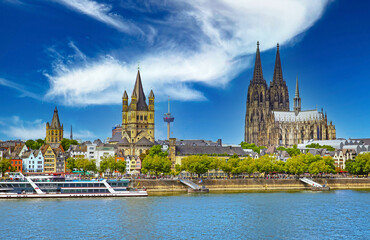 Cologne, Germany - July 9. 2022: Spectacular riverfront skyline. three churches, dome, rhine cruis ship, clear blue summer sky, white cloud, TV tower