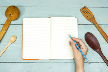kitchen utensil with blank recipe book and woman hand holding a pencil 