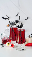 Close-up of two bloody cocktails glass goblets for Halloween,bottle form skull,candy eyes,bats,spiders,pumpkins white background.Decor concept for Halloween party,alcoholic drinks,cranberry punch