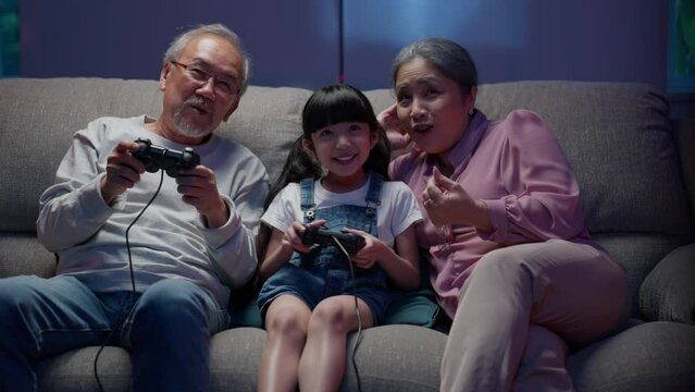 Happy family spending time together at home, Little girl playing video games with family, Senior grandfather and grandmother enjoying to play games with granddaughter in the living room