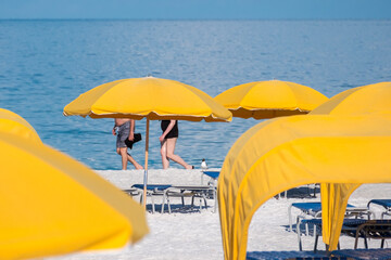 People walking on the beach partially obscured by bright yellow cabanas and umbrellas