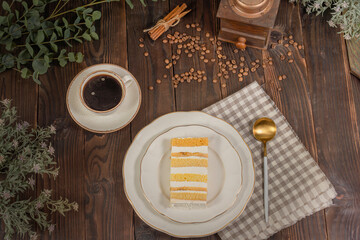 A piece of cake with banana filling, a cup of hot coffee and cinnamon on a wooden table, top view. Sunday morning breakfast and rest.