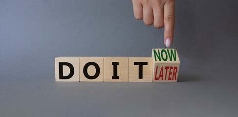 Do it now or later symbol. Businessman hand points at wooden cubes with words Do It Later and Do It Now. Beautiful grey background. Business concept. Copy space