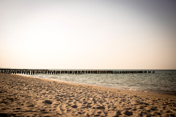 Plaża nad polskim morzem na tle zachodzącego słońca z falami i falochronem