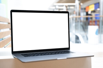 Laptop with white screen in business office or shopping mall. Empty copy space, blank screen mockup. Soft focus laptop with interor background. Travel, study and office work concept