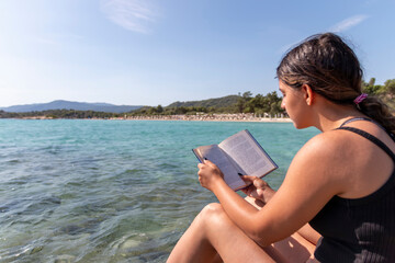 Teen girl reading a book and relaxing at the beach