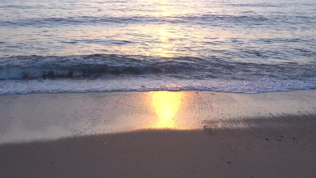 Ondas com reflexo do p&ocirc;r do sol na areia da praia