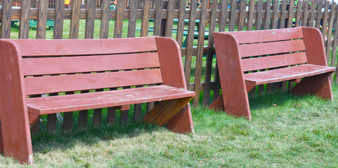 Two wooden sitting benches along fence