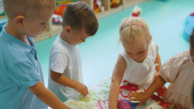 Sensory play at nursery school. Toddlers with their teacher having fun with white, fluffy cloud dough, and using modeling tools such as colorful and textured rolling pins, cutters, silicone shape