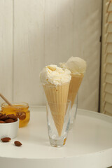 Delicious vanilla ice cream in wafer cones with honey and almonds on white table indoors