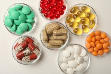 Different dietary supplements in bowls on white background, flat lay