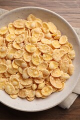 Bowl of tasty corn flakes on wooden table, top view