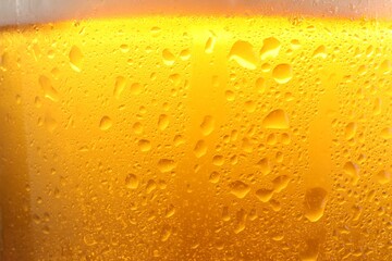 Glass of tasty cold beer with foam and condensation drops as background, closeup