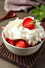 Delicious strawberries with whipped cream served on wooden table, closeup