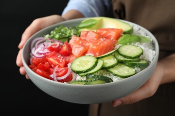 Woman holding delicious poke bowl with salmon and vegetables on black background, closeup