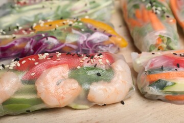 Delicious rolls wrapped in rice paper on wooden board, closeup