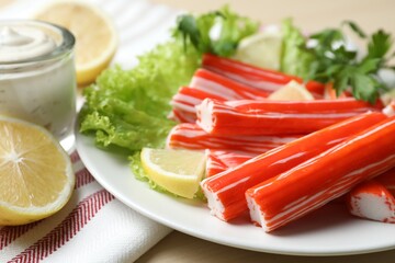 Delicious crab sticks with lemon and lettuce on table, closeup