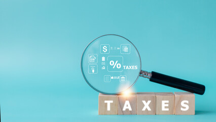 Magnifier glass with the icon of tax concept on the wooden cube. Business concept