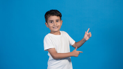 Hermoso niño con playera blanca, gafas de sol y fondo azul señalando con el dedo, ambas manos.