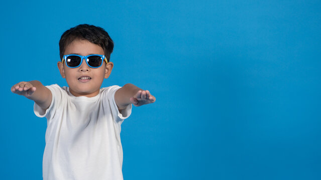 Ni&ntilde;o guapo con lentes de sol actuando como zombi con playera blanca y fondo azul