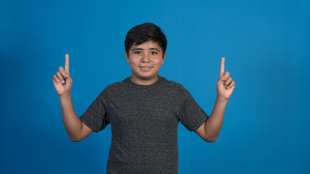 Foto de chico alegre llevar ropa de moda haciendo aislada en el fondo de color azul. Señalando con su dedo hacia arriba.