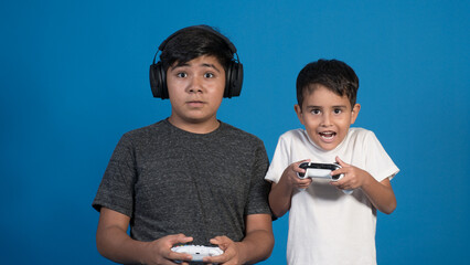 Retrato de estudio de dos niños jugando a videojuegos con auriculares y joystick. Posando en fondo...