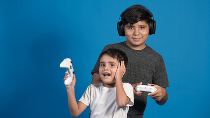 Retrato de estudio de dos niños jugando a videojuegos con auriculares y joystick. Posando en fondo Azul.