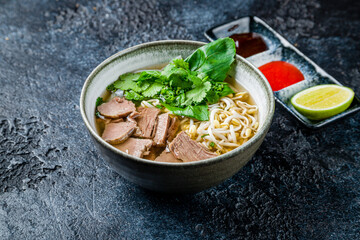 Soup Pho Bo with beef, mint and noodles on dark stone table