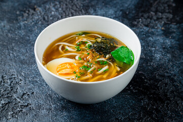 Chicken soup bouillon in a plate with egg and noodles on dark stone table