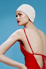 A retro-style swimmer in a red swimsuit holds her hands at the waist on a blue background. Fashion...