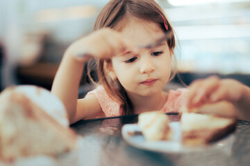 Toddler Girl Focused on Eating on a Restaurant. Little child feeling food after eating in a...