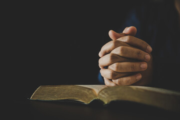 Hand folded in prayer to god on Holy Bible book in church concept for faith, spirituality and...