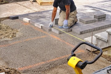 Landscaping contractor worker using tape measure ruler measuring and laying interlock stones on a construction site.  - obrazy, fototapety, plakaty