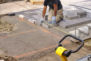 Poster Landscaping contractor worker using tape measure ruler measuring and laying interlock stones on a construction site.  © VisualArtStudio