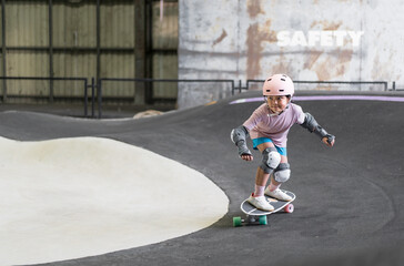 asian child skater or kid girl fun playing skateboard or ride surf skate and turn on pump track in skate park by extreme sports to wearing helmet elbow pads wrist knee support for body safety protect © kornnphoto