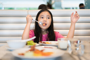 Asian child or kid girl enjoy eating carrots by fork and vegetables salad with variety foods or...