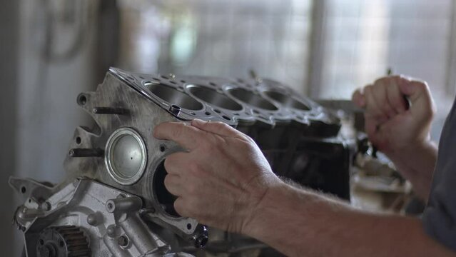 Repairman Screws Broken and Disassembled Car Engine on Bench with Two-Head Wrench in Repair Shop Footage.