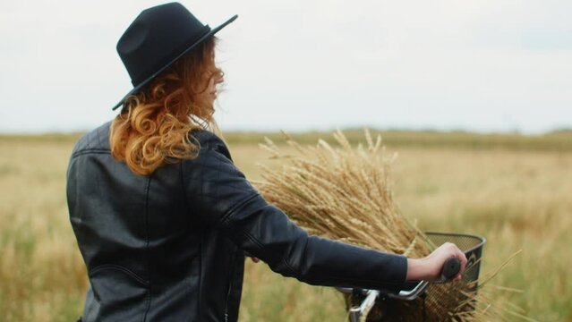 Woman with crops looking away while walking with bicycle. Young female is wearing casuals in farm during windy weather. She is spending leisure time in agricultural field.